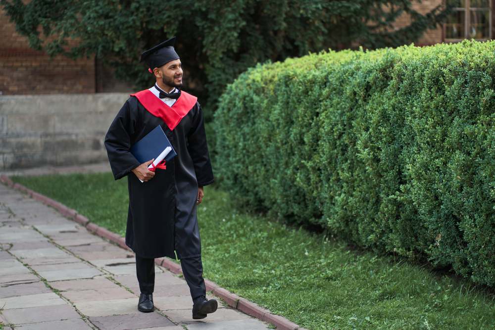 A man from India graduating from college in a cap and gown holding his diploma